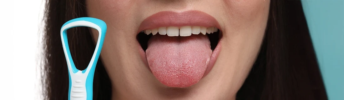 Dentist Lewiston ME Bad Breath close up of a woman holding a tongue scraper while sticking out her tongue
