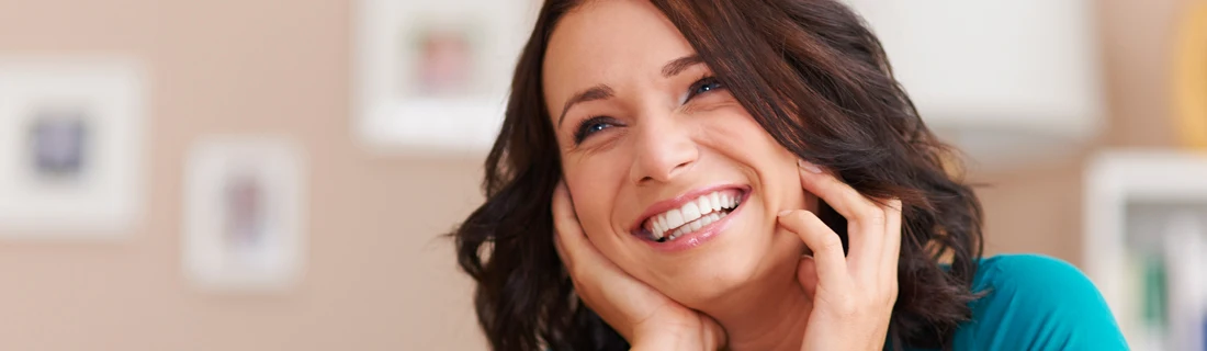 Dentist Lewiston ME Cosmetic Dentistry Focused beautiful woman with brown hair smiling while holding her head in her hands