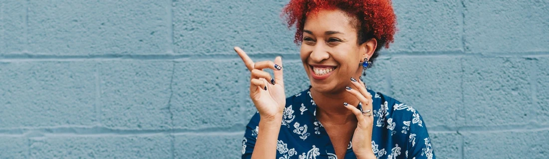 Dentist Lewiston ME Dental Veneers Focused woman with short vibrant red hair and dark toned skin is laughing and pointing upward