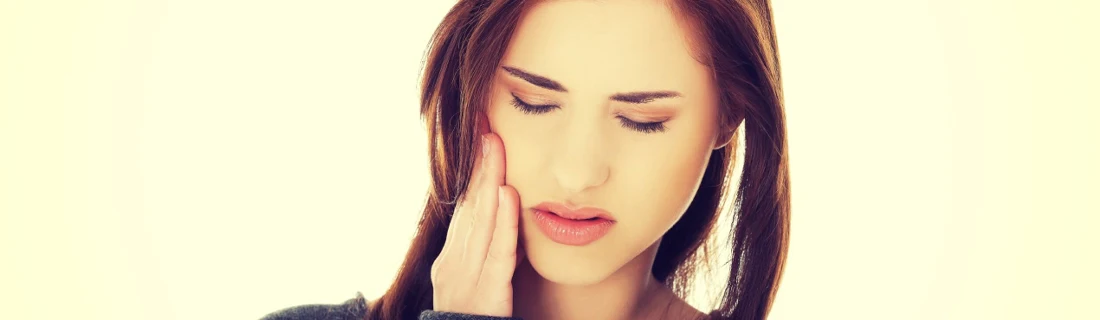 Dentist Lewiston ME Tooth Infection woman holding her jaw wincing in pain against a soft yellow background
